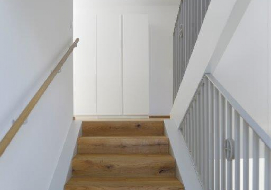 Der Treppenaufgang wurde mit Holzstufen ausgeführt um dem schlichten, in weiß gehaltenen Inneren Wärme zu verleihen.