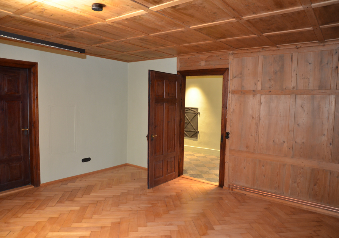 Raum im Obergeschoss mit Holzdecke, getäferten Wänden und Fischgrätparkett